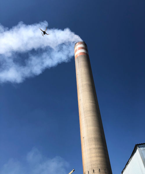Drone inspecting a tall industrial chimney